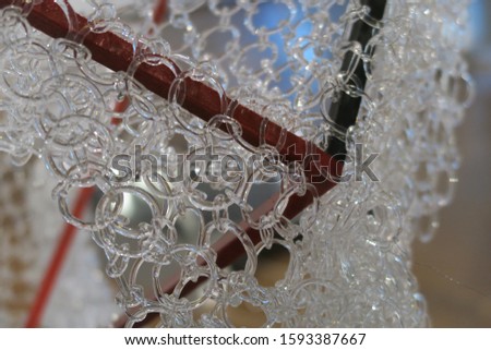 A closeup photo of a construction hanged on metal rods, made from small circular chains of thin transparent glass