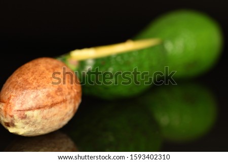 In the photo are located diagonally: one whole avocado bone, in focus. Behind it is a half, cut along, a green, ripe avocado. In the background is one, a whole avocado