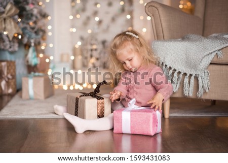 Pretty child girl 3-4 year old open Christmas present sitting on floor in room over Christmas decor closeup. New Year. Childhood. Winter holiday season. 