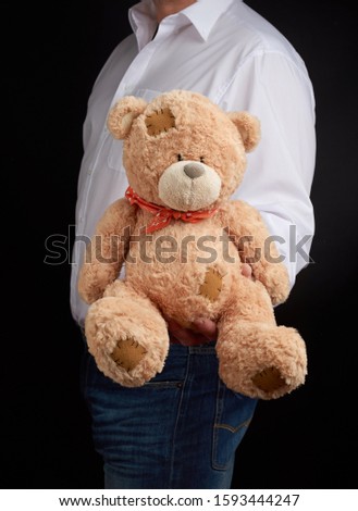 man in a white shirt holds a large teddy beige bear with patches, concept of a gift for Valentine's Day