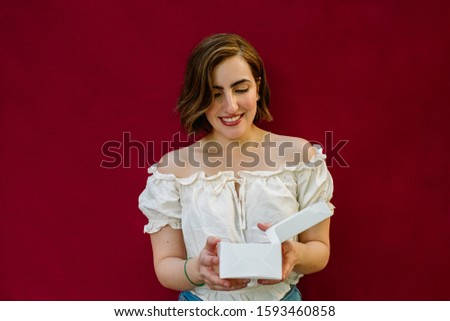 happy young woman opening a white box on red background