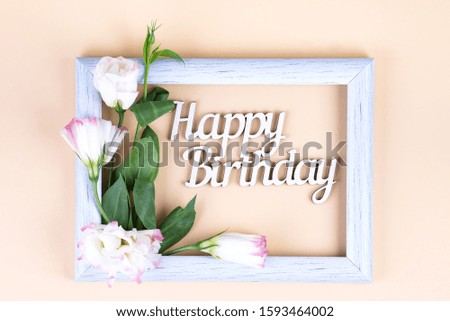 Empty white frame and flowers eustoma on beige paper background with copy space. Birthday concept