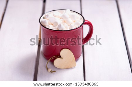 red mug with marshmallows and a Christmas decoration in the form of a heart on a light background