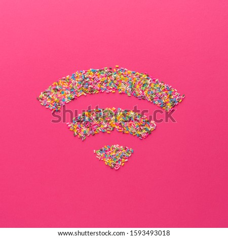 Wifi signal symbol made of colorful sugar sprinkles on pink background in minimal style. Top view flat lay image.