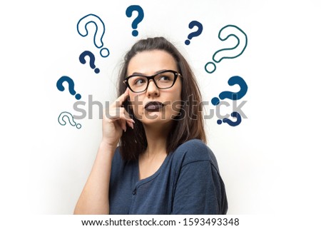 Portrait of a beautiful girl on a white background with question marks, looks aside with pensive expression, is considering a plan for further action.