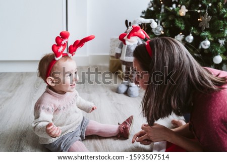 mother and cute baby girl playing at home with reindeer diadem. Christmas concept