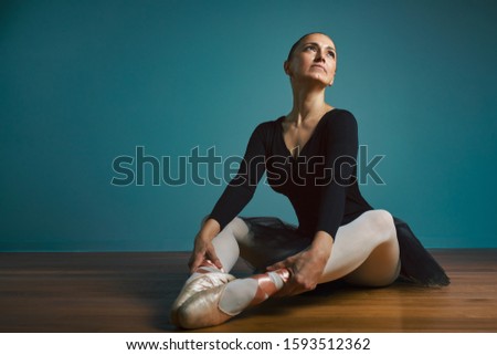pretty woman ballerina in tutu and pointe in black swimsuit posing in studio on blue background