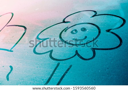Smiley face flower freehand drawing above a blue ocean color dirty tail car window glass texture with finger dust for background with copy space waiting for water clean or car wash business concept