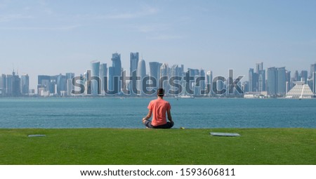 A man meditates and relaxes on the hill of the MIA park in Doha Qatar over looking the city skyline Royalty-Free Stock Photo #1593606811