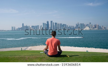 A man meditates and relaxes on the hill of the MIA park in Doha Qatar over looking the city skyline Royalty-Free Stock Photo #1593606814