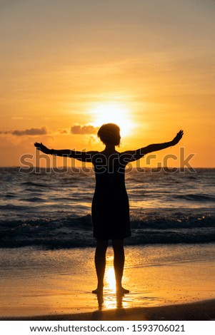 silhouette of one girl on the background of the sunrise on the beach. The girl stands facing the ocean with her arms outstretched and rejoices in a new day