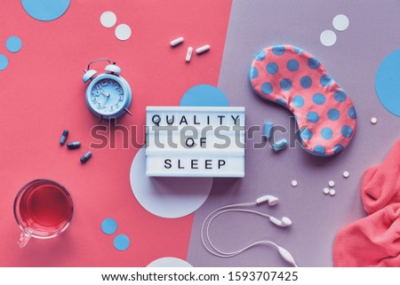 Healthy night sleep creative concept. Sleeping mask, blue mint alarm, earphones, earplugs. Two tone pink and silver background with paper circles. Flat lay, lightbox with text "Quality of sleep".