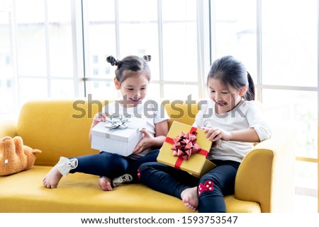 A 6 and 4 year old Asian girl Sitting on yellow sofa, are happiness and excited Because received a pleasant gift On the New Year's Day festival, to children and holiday concept.