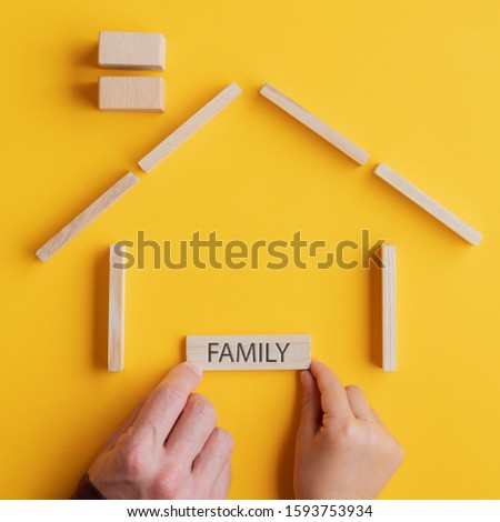 Child and son placing a wooden peg with Family sign on it in a house made of wooden blocks in a conceptual image. Over yellow background.