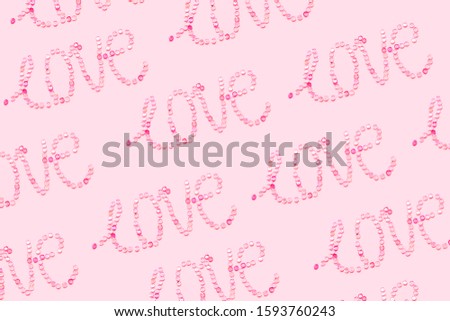 love written with sequin in open composition pattern on a pastel pink background