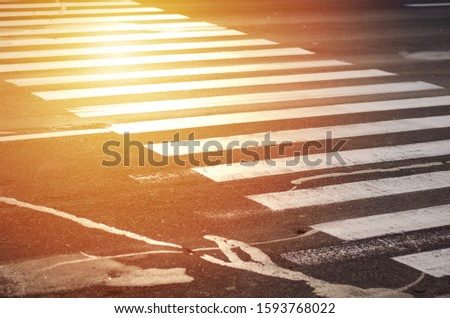 Zebra pedestrian crossing. Patched asphalt. Not a very safe crossing over a wide road. Sunlight.