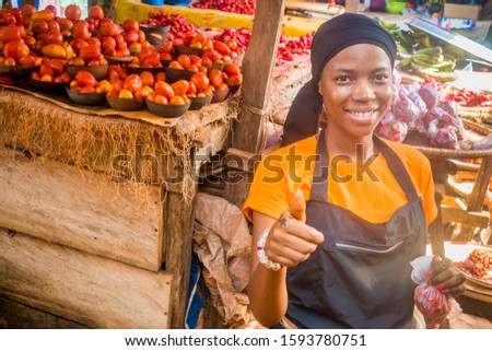 young african woman selling tomatoes in a local african market smiling an giving thumbs up gesture