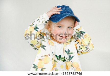 Happy childhood.  Emotional portrait of a kind and positive beautiful little girl with blond hair and a denim cap, looking with a smile at the laptop screen while watching a cartoon, isolated on white