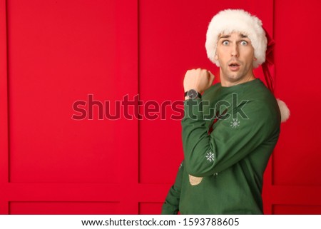 Surprised young man in Santa hat and with watch on color background. Christmas countdown concept