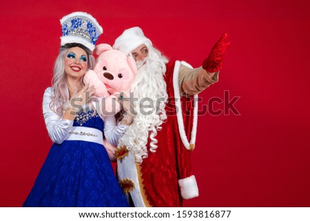 Emotional Santa Claus in a red coat and Snow Maiden in a blue suit posing on a red background