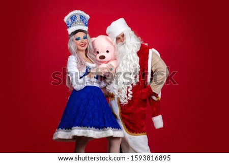 Emotional Santa Claus in a red coat and Snow Maiden in a blue suit posing on a red background