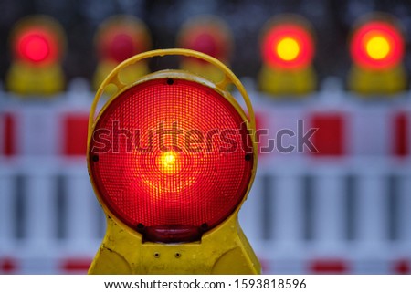 Closeup of a red warning light glowing in the dark at a construction site with street barriers in Germany in December