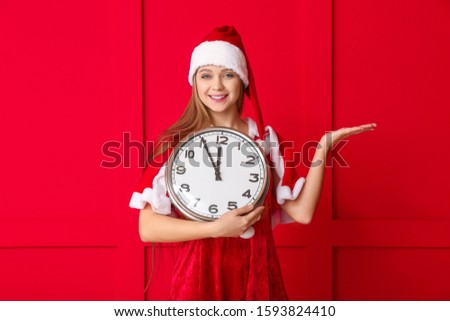 Young woman in Santa costume and with clock on color background. Christmas countdown concept