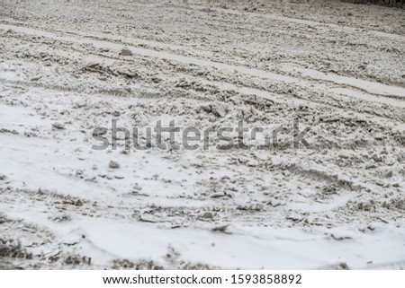 Black car driving at snowfall. Close-up at dirty wet road with pedestrian crossing. Dirty, melted snow with cars and shoes prints. Motion blur.