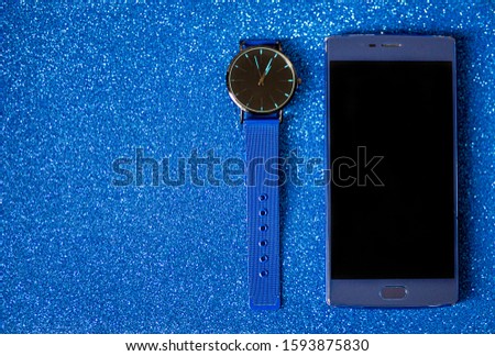 blue wristwatch and blue smartphone on a blue background, hipster fashion, view from above, business concept, space for text