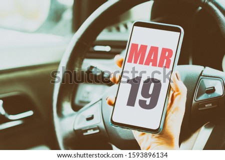 march 19th. Day 19 of month,Calendar date. Month and day placed on a smartphone screen in womans hand in car interior. artistic coloring.  spring month, day of the year concept