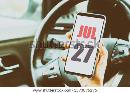 july 27th. Day 27 of month,Calendar date. Month and day placed on a smartphone screen in womans hand in car interior. artistic coloring.  summer month, day of the year concept