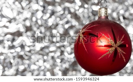 Vintage decorative christmas bauble in red color with large decorative stars  against a silver bokeh blurry star background.