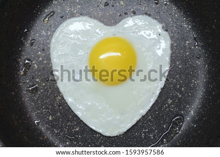 Stock photography fried eggs in the shape of a heart in a black pan. Valentine's day breakfast festive concept. 