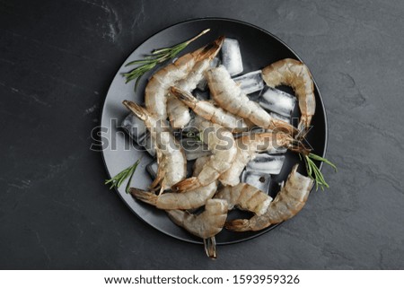 Fresh raw shrimps with rosemary and ice cubes on black table, top view