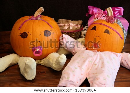 Two pumpkins dressed up as princess babies with pacifiers on a table beside gifts.