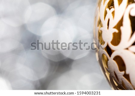 Vintage decorative christmas bauble in yellow color with a decorative white pattern against a silver bokeh blury star background.