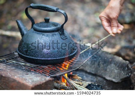 Boiling water. Large metallic black kettle in ash. Basking at the stake. Wooden firewood burns and smokes. 
