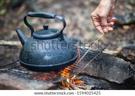 A woman sets fire to an aroma stick. The human hand.Boiling water. Large metallic black kettle in ash. Basking at the stake. Wooden firewood burns and smokes.