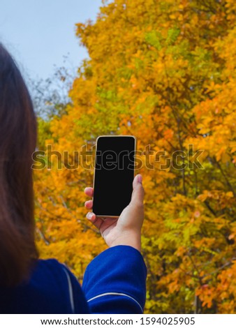 A woman with a phone to take pictures of leaves