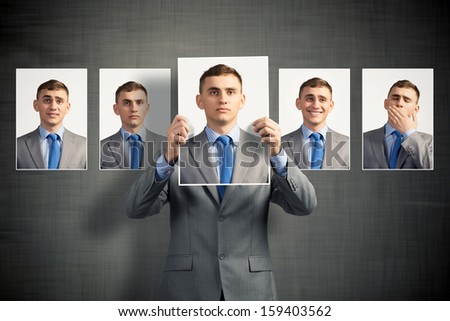 young man holds up a photograph hanging on the wall behind the additional photos with different emotions