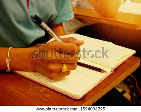 Student using a pen and pencil doing writing assignment in a lecture room, selective focused picture of learner taking creative writing class in school, college, or university campus, education image