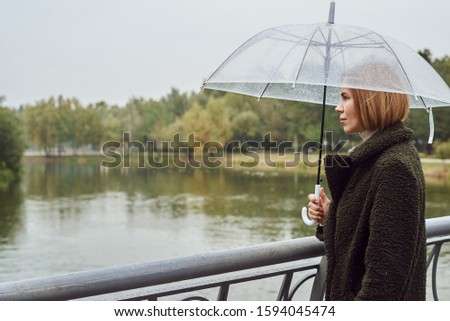 Woman under an umbrella in the autumn in the park. Autumn landscape, rain, bad weather. The concept of loneliness, sadness, reflection.