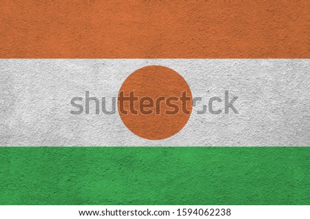 Niger flag depicted in bright paint colors on old relief plastering wall. Textured banner on rough background