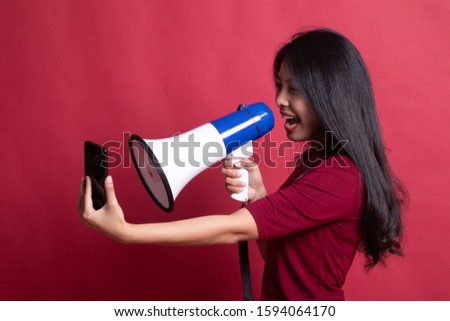 Angry  young Asian woman shout with megaphone to mobile phone on red background.