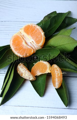 half of peeled tangerine tangerine, slices of tangerine and green leaves isolated on wooden white background. vertical picture