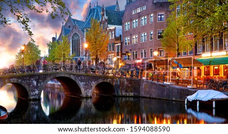 Red-light district in Amsterdam city picturesque landscape panorama evening town with pink sunset sky. Bridge over canal river Amstel.