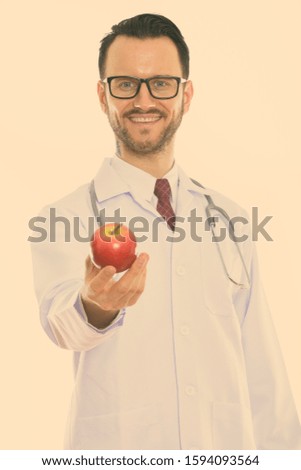 Studio shot of happy young man doctor smiling while giving red apple