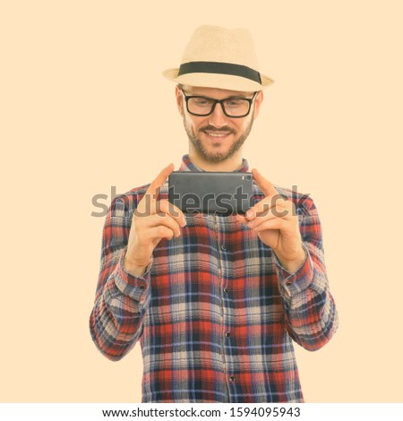 Studio shot of happy young man smiling while taking picture with mobile phone