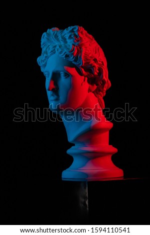 Plaster statue of a bust of Apollo Belvedere in red and blue light on a black background