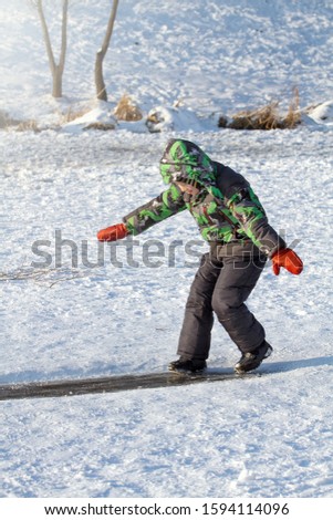 Boy Have Fun Outdoors In Winter. Boy Are Sliding on Ice Rink Trying Not To Fall Down
